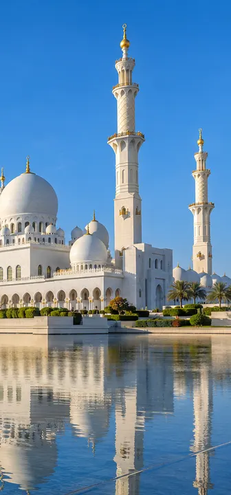 Sheikh Zayed Grand Mosque in Abu Dhabi with its white domes reflected in the pool, under a clear blue sky