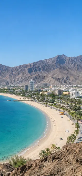 The curved sandy beach and blue bay of Khorfakkan with mountains behind